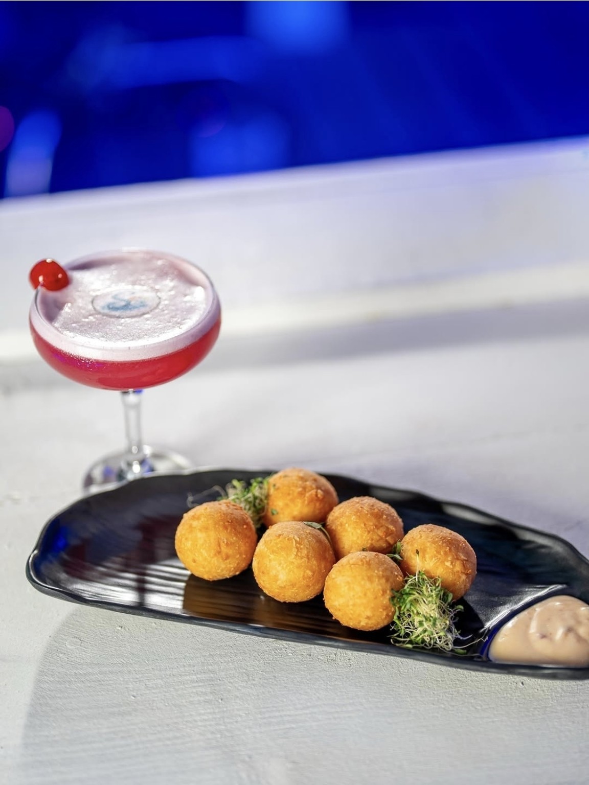 Golden cheese balls with dipping sauce beside a pink cocktail at Santorini
